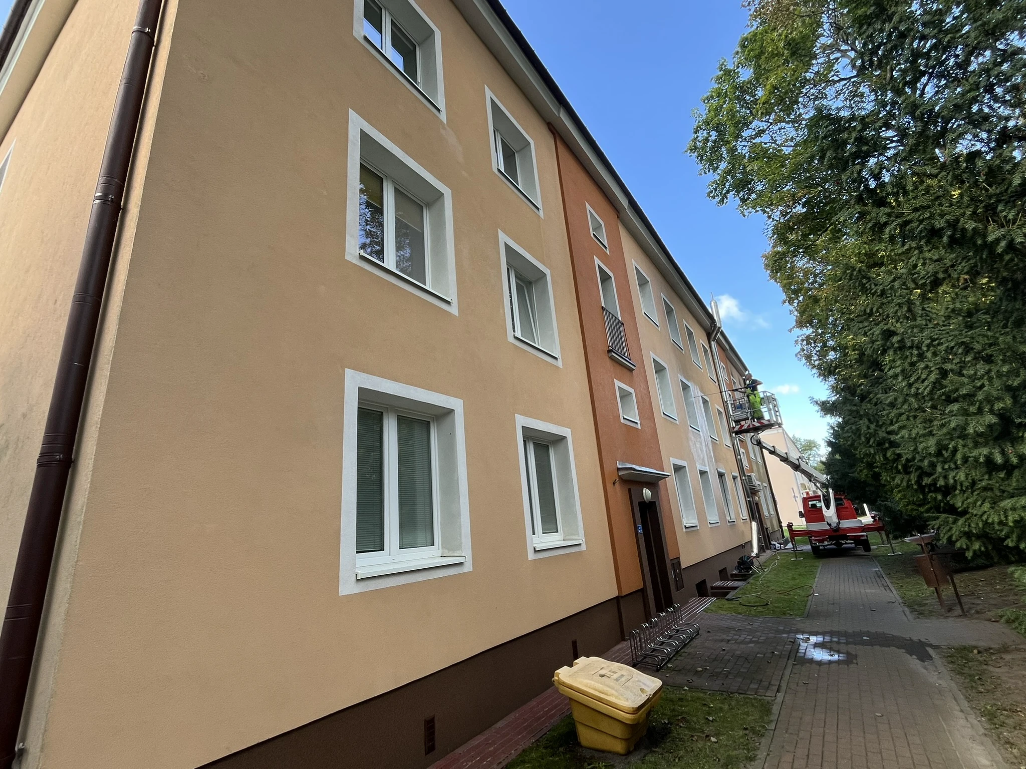 Mycie elewacji pastelowego, trzykondygnacyjnego budynku z użyciem podnośnika koszowego