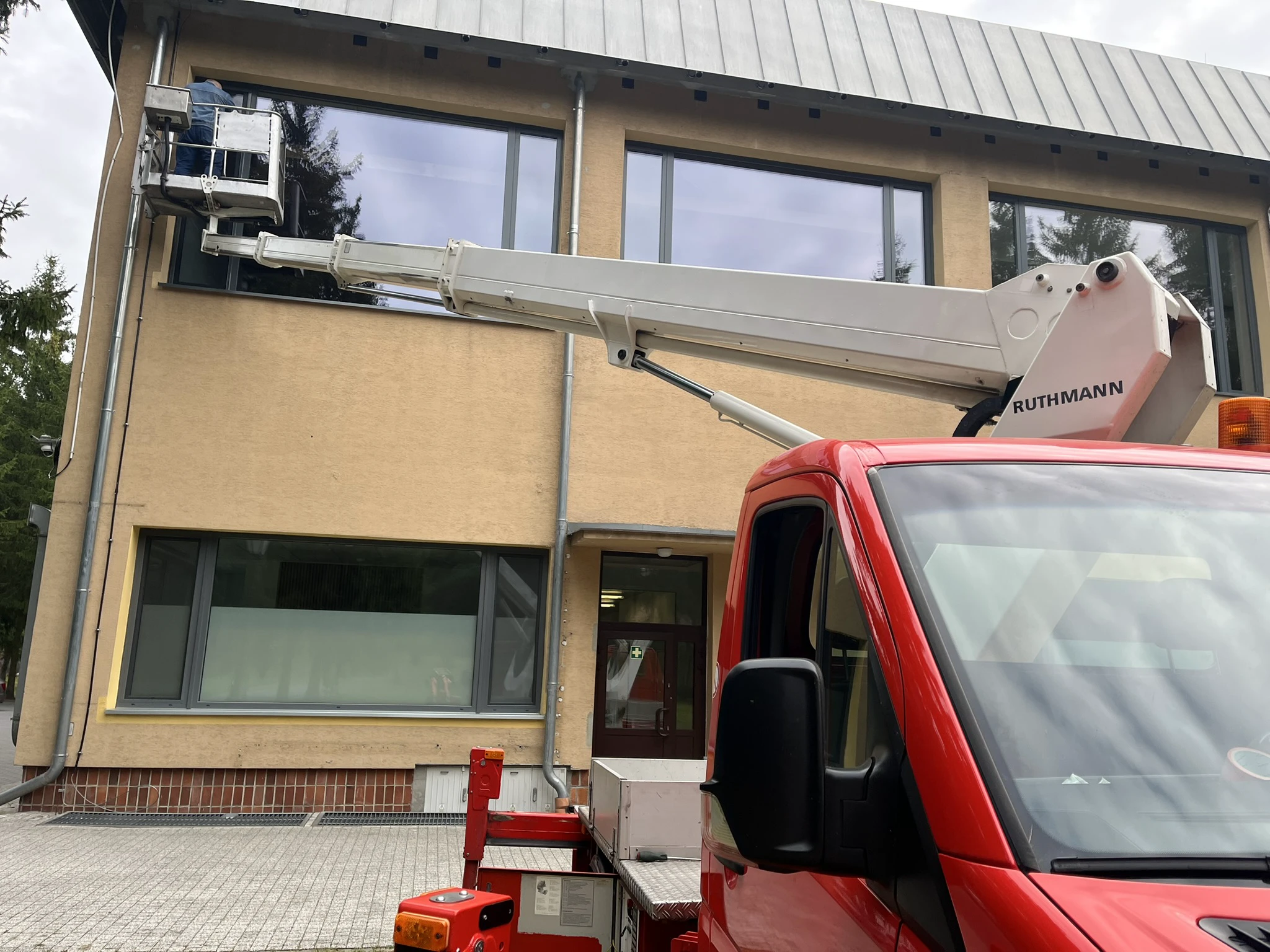 Czerwony samochód z podnośnikiem koszowym przy elewacji budynku podczas usług podnośnikiem koszowym