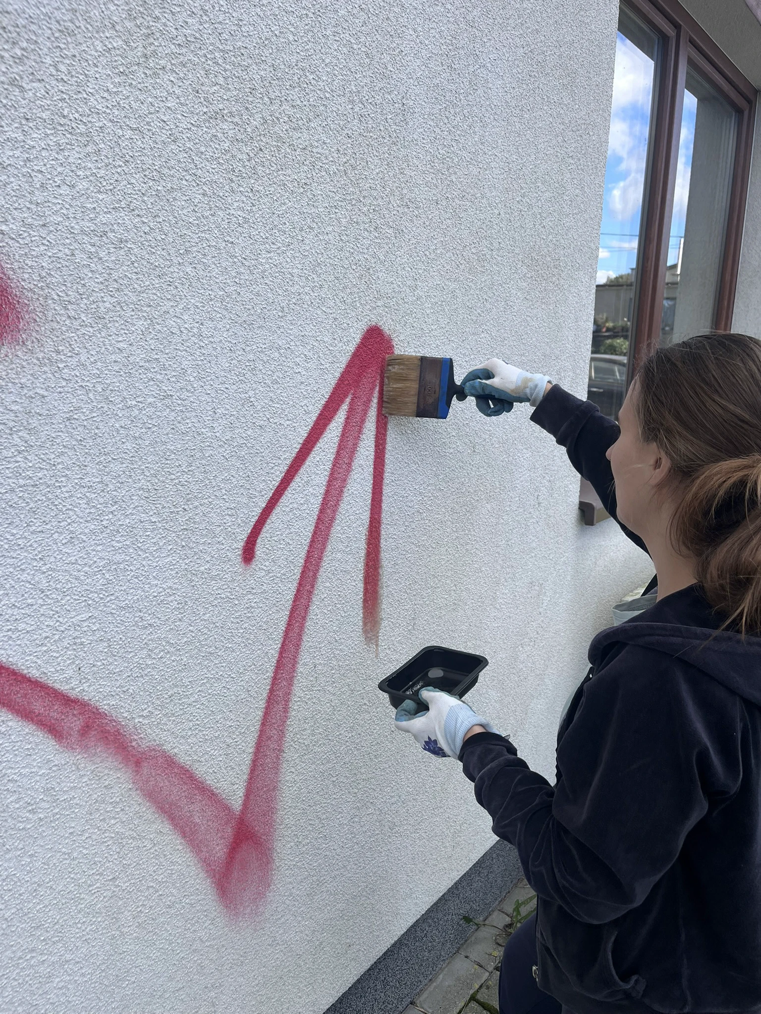 Pracownik pędzlem maluje białą farbą elewację, wykonując usługę Usuwanie graffiti