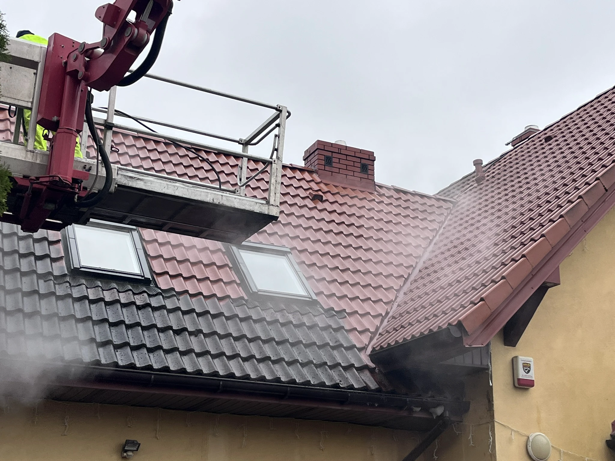 Pracownik na podnośniku koszowym czyści dachówkę myjką ciśnieniową – mycie dachu