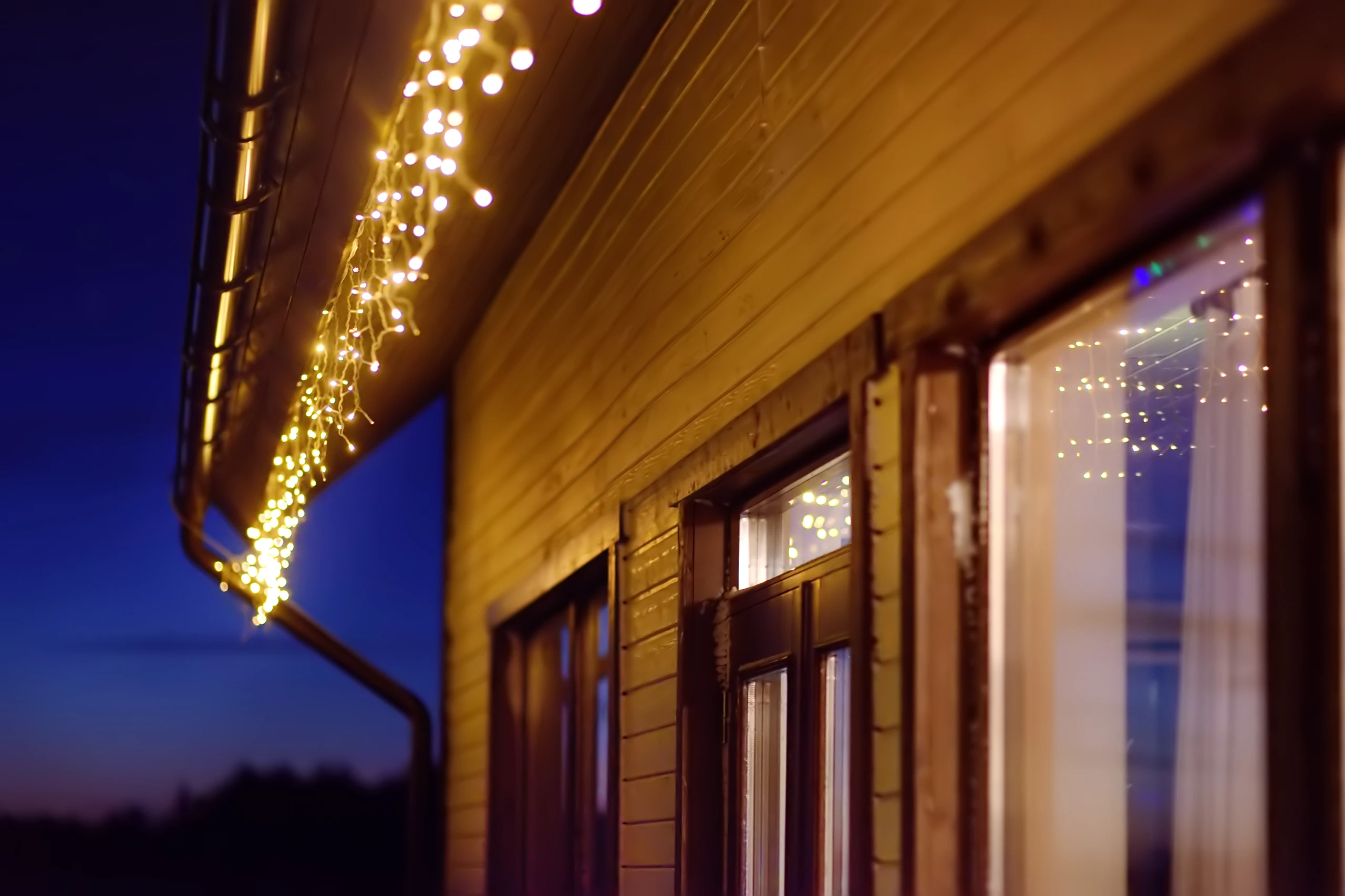 Montaż iluminacji świątecznych na drewnianej elewacji domu przy oknach